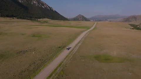 A camper drives through a vast open valley near mountains on Beartooth Stock Footage 286845798