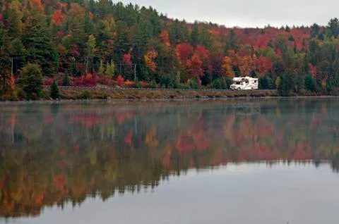 Camper driving though fall forest with colorful autumn leaves reflecting in l Stock Photos