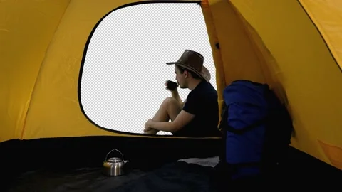 Camper in hat is resting and drinking tea near tent with rucksack, alpha channel Stock Footage 159793254
