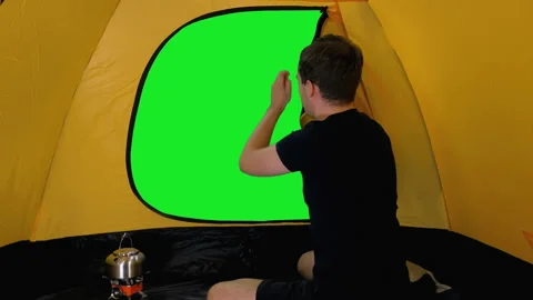 Camper opens tent sitting inside and looks out on green screen background Video stock 159791174