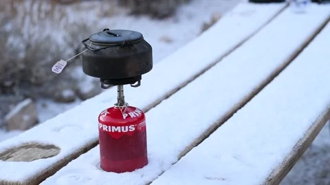 Camper Pours Hot Tea From Kettle Into Metal Mug on Snowy Picnic Table Stock Footage 300825491