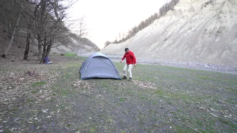 Camper Setting Up Camp by River in Mountainous Terrain 動画素材 303664546