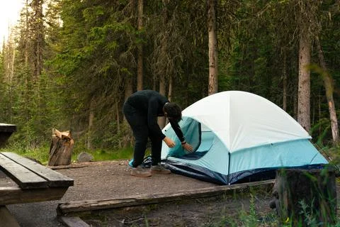 Camper setting up a tent in the woods, preparing for a night of camping. Stock Photos