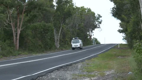 Camper van driving away on empty wide road in forest, handheld footage Stock Footage 132172198
