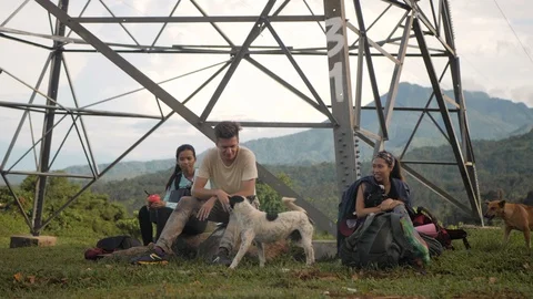 Campers sitting on the rocks under a tower at the mountain, playing with dogs. Stock Footage 116354794