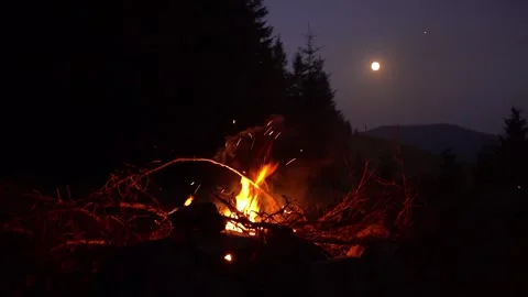 Campfire Burning Against a Mountain Landscape Under a Full Moon at Night 스톡 동영상 339774399