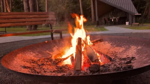 A campfire burns brightly in a fire pit surrounded by wood logs. Benches stand Stock Footage 341491903