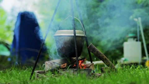 Campfire cooking in cast iron pot with smoke rising over fire outdoors at Stock Footage 339865596
