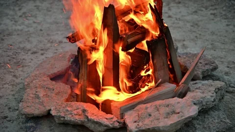 Campfire flames rise from stacked logs in stone fire pit at dusk Stock Footage 340251334