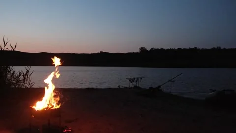 Campfire with gentle flames beside a river during sunset Stock Footage 243400653