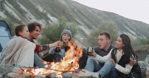 Campfire group of friends sitting down and drinking tea or some hot drinks Video stock 102643195