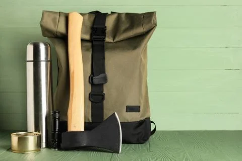 Camping backpack with an axe, thermos, flashlight, and canned food on a green Stock Photos