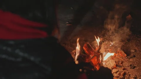 Camping campfire stoking at night, camper actively tending coals with stick and Stock Footage 345159960
