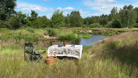 Camping chairs and a picnic table line the riverbank in summer Stock Footage 333188408