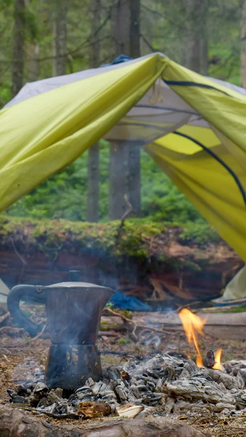 Camping coffee pot heating on campfire near tent in forest Stock Footage 334998885