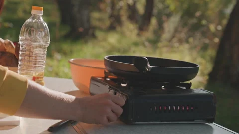 Camping frying pan white hands turning knob and pouring oil, skillet warming on Stockbeeldmateriaal 332287677