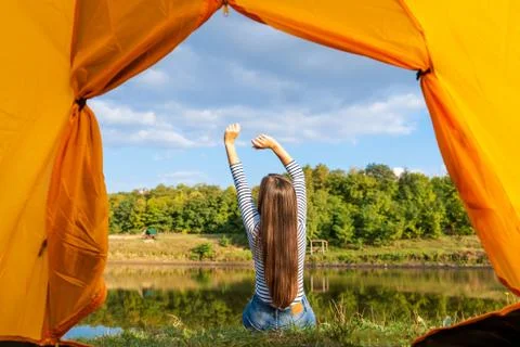 Camping on lake shore at sunset, view from inside tourist tent. Girl enjoy na Stock Photos