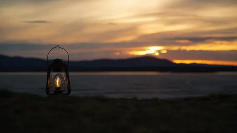 A camping lantern burning on the shore of a lake at sunset. 스톡 동영상 333206071