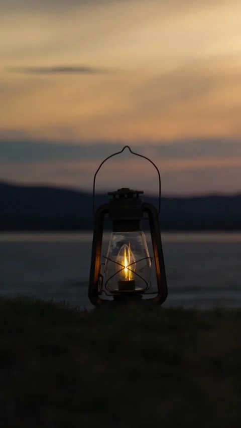 A camping lantern burning on the shore of a lake at sunset. Vídeo Stock 344021698