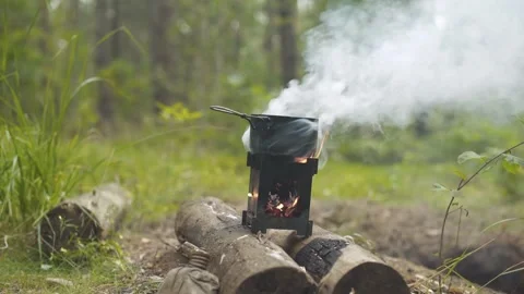 A camping pot standing on a portable folding wood stove in the forest. 스톡 동영상 280226632