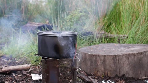 Camping pot steaming over open fire on portable stove at rustic campsite 動画素材 337212718