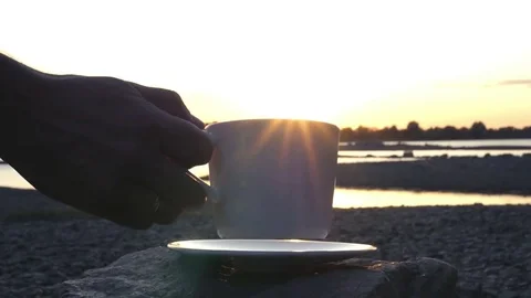 Camping by the river at sunset, putting a cup of hot tea on a stone and a saucer Stock Footage 80987162