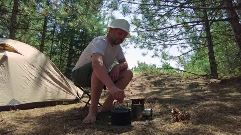 Camping Scene: Man Taking Kettle Off Wood Stove in Pine Forest Stock Footage 282239760