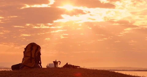 Campside with Backpack, bonfire, coffee cup, morning sunset landscape, Stock Footage 119995370