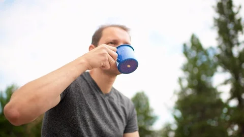 Campsite with man closeup drinking tea from mug cup in morning by firepit Stock Footage 120608919