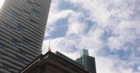 Canadian flag at half-mast between modern towers, moving clouds overhead Stock Footage 320017771