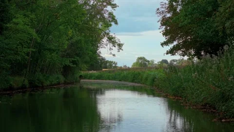 Canal winding through forest edge with cloudy sky reflected in water. Autumn Stock Footage 317082358