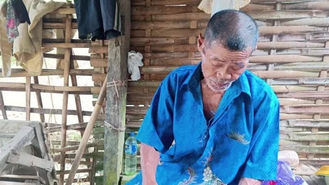 Candid Elderly Farmer Having a Snack Break Inside Traditional Bamboo Wooden Hut Stock-Footage 335019498