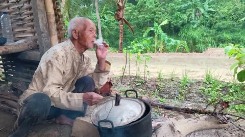 Candid Elderly Farmer Lighting Cigarette with Wooden Stick from Traditional Stov Stock-Footage 335019487