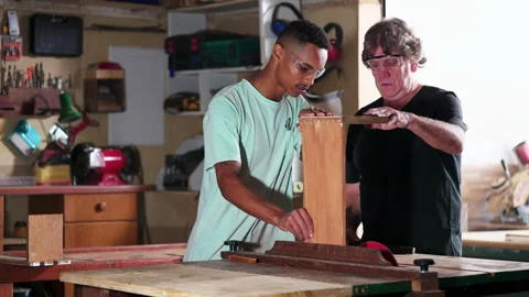 Candid senior carpenter guiding apprentice to use saw machine, slicing piec.. Stock Footage 247280225