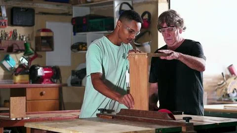 Candid senior carpenter guiding apprentice to use saw machine, slicing piec.. 스톡 사진