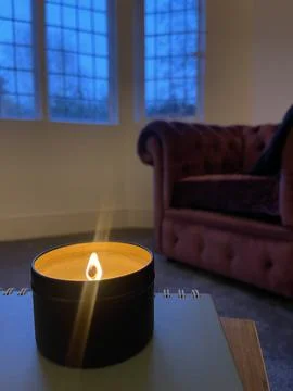 Candle burning on the table during dusk, comfortable vintage armchair in the  Stock Photos