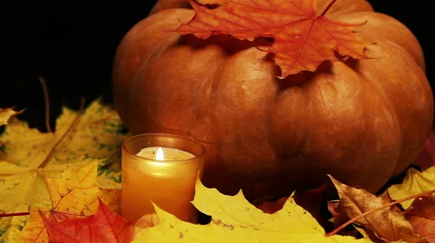 The candle burns before pumpkin and maple leaves on dark background Stock Footage