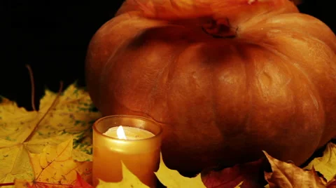 The candle burns before pumpkin and maple leaves on dark background Stock Footage