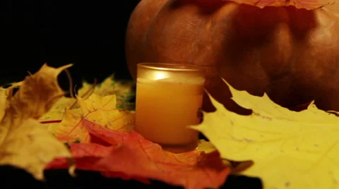 The candle burns before pumpkin and maple leaves on dark background Stock Footage
