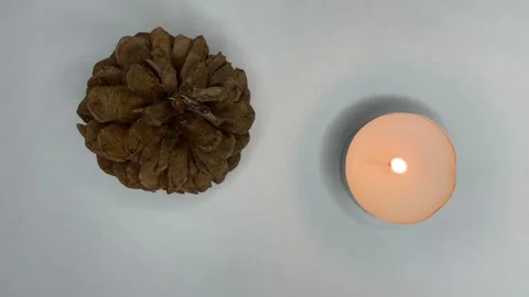 A candle burns on a white background, a forest cone lies nearby Stock Footage 252188698
