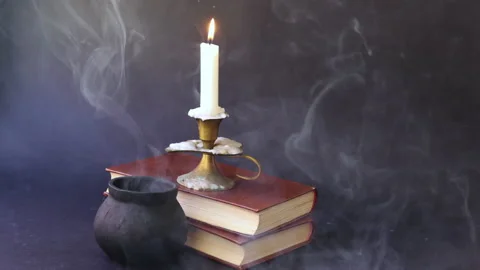 Candle in candlestick burning on old books and smoky pot Stock Footage 137870518