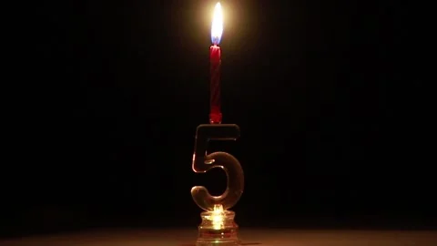 Candle on candlestick in the form of number five burns on a black background Stock Footage 151311670