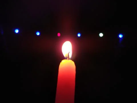 A CANDLE FLAME GIVE LIGHT IN DARK NIGHT WITH LIGHT BILINKING BEHIND Stock Photos