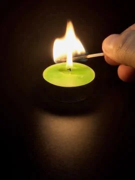 Candle lights up from a match on a black background Stock Photos
