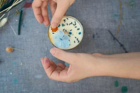 Candle maker adding decorative dried flowers to handmade candle in craft Stock Photos