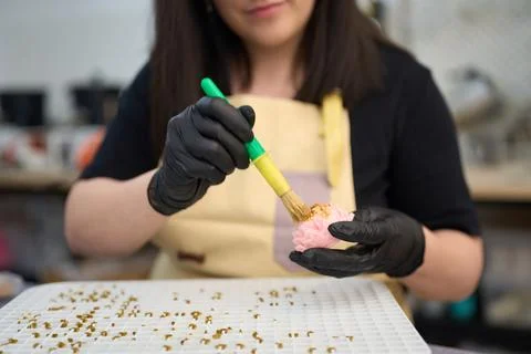 Candle maker applying gold leaf to pink flower-shaped candle Stock Photos