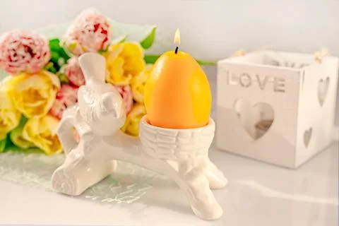 Candle in the shape of an egg with a burning wick and spring tulips on a li.. Stock Photos