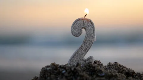 Candle in shape of number two 2 burning background of blue sea sand seashore Stock Footage 255571692