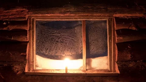 A candle thaws the frozen window of a small log house 4K timelapse Video stock 77146591