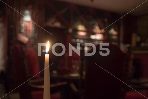 Candle in winery, blurred red chairs in background with bottle of wine Stock Photos